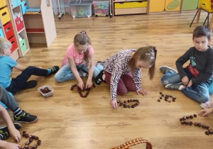 Dzieci układają kształt wielkiej i małej litery A z kasztanów.